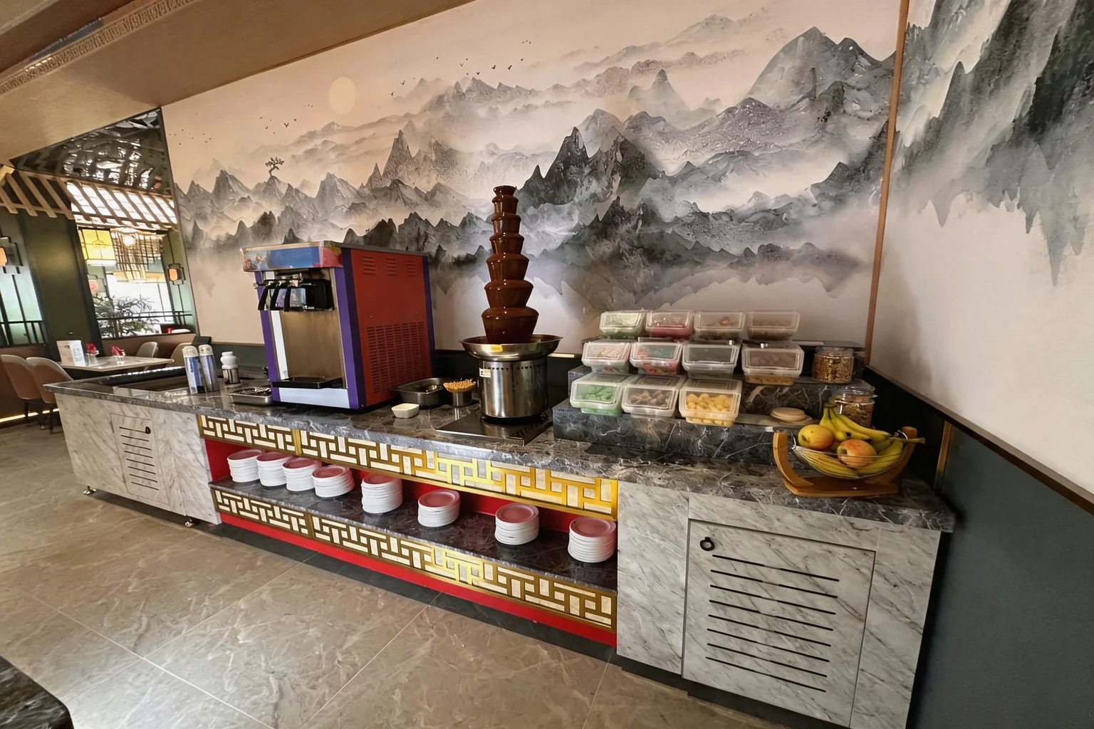 Fontaine au chocolat et machine à glace sur le buffet, devant une fresque de montagnes à l'encre chinoise