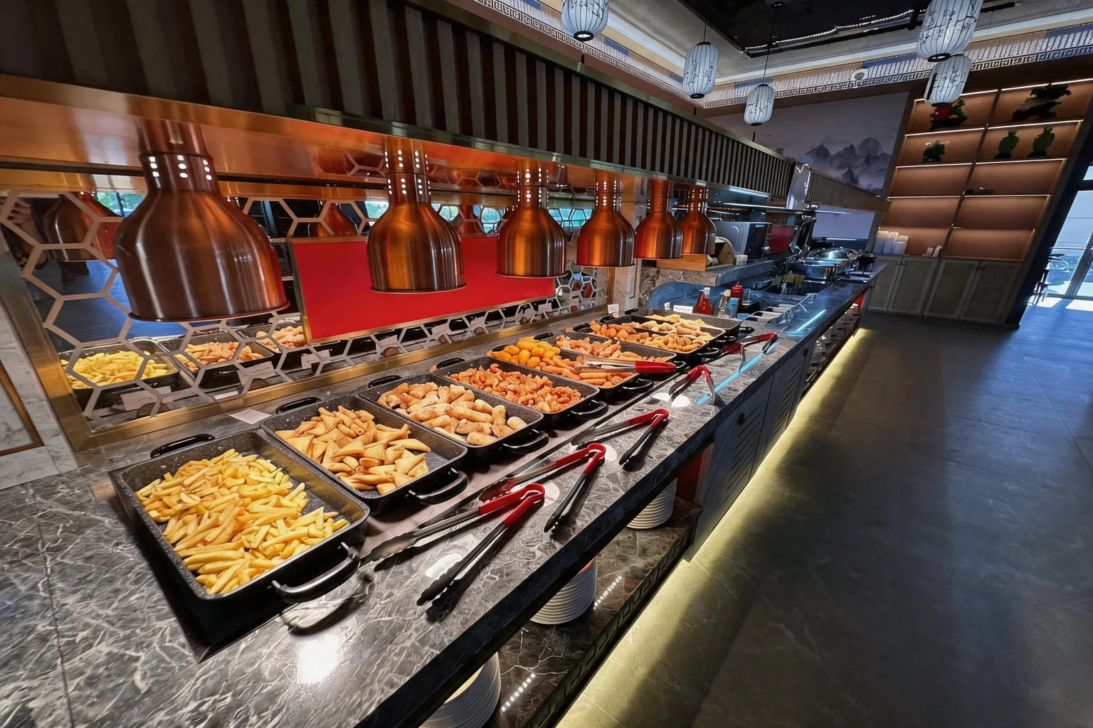 Bacs de frites, samoussas et nems au poulet sur le comptoir du buffet, sous des suspensions en cuivre