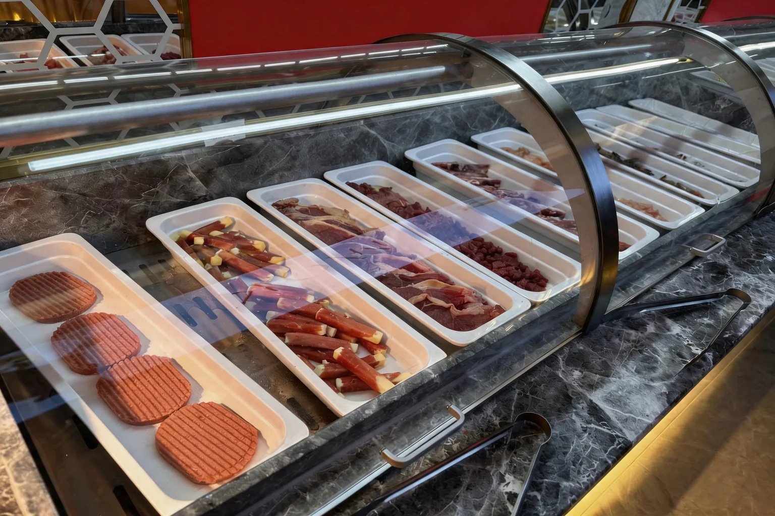 Bacs de viandes crues variées présentés sous vitrine sur le buffet, prêtes à griller